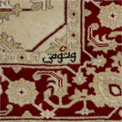 Baluchi signed hand-knotted rug, ivory ground, with an all-over geometric lattice design incorporating stylised flowerheads, hooked motifs and angular vine work, enclosed by a crimson border with repeating floral motifs and scrolling vines, flanked by narrow patterned guard stripes, signed to one corner, with cotton fringes