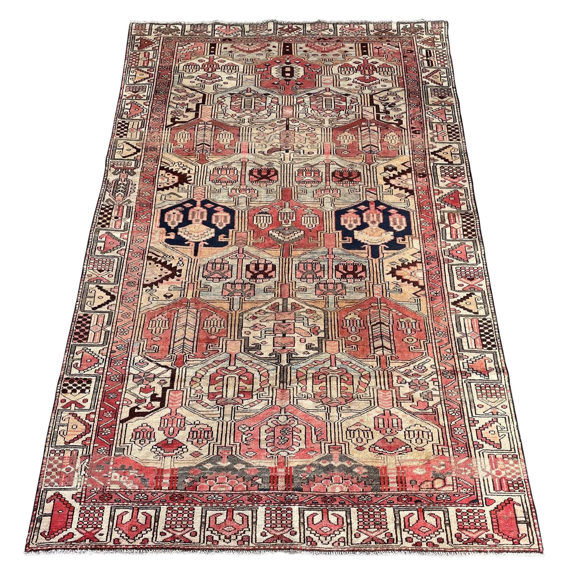 Persian Heriz red and pale ground rug, depicting multiple shaped panels with stylised motifs and designs, geometric patterned border
