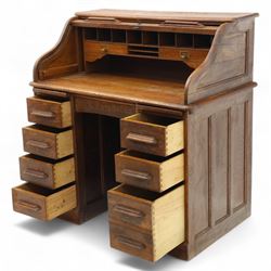 Early 20th-century oak roll-top desk with tambour shutter, enclosing a fitted interior of pigeon holes and small drawers, and pedestal base fitted with nine drawers with moulded handles, raised on plinth base 