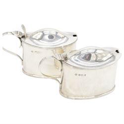 Pair of Edwardian silver mustard pots, of oval form with reed borders and palmette thumb pieces to hinged covers, opening to reveal blue glass liners, hallmarked William Hutton & Sons Ltd, London 1905, H7.5cm