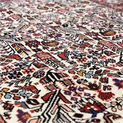 North west Persian Rudbar hand-knotted rug, ivory field woven with a repeating pattern of stylized shrubs, rosettes, and geometric floral motifs in tones of madder red, turquoise, indigo, and ochre, enclosed by a border of linked rosettes and angular flowerheads between narrow guard stripes 