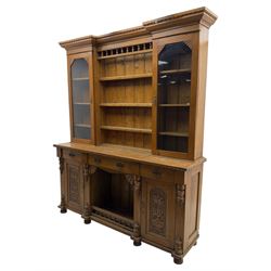 Late 19th century pine dresser, the projecting cornice with dentil and spindle moulded frieze above a three-tier plate shelves, flanked by glazed doors, the base fitted with three frieze drawers over arched apron and carved floral panelled cupboard doors, raised on turned feet