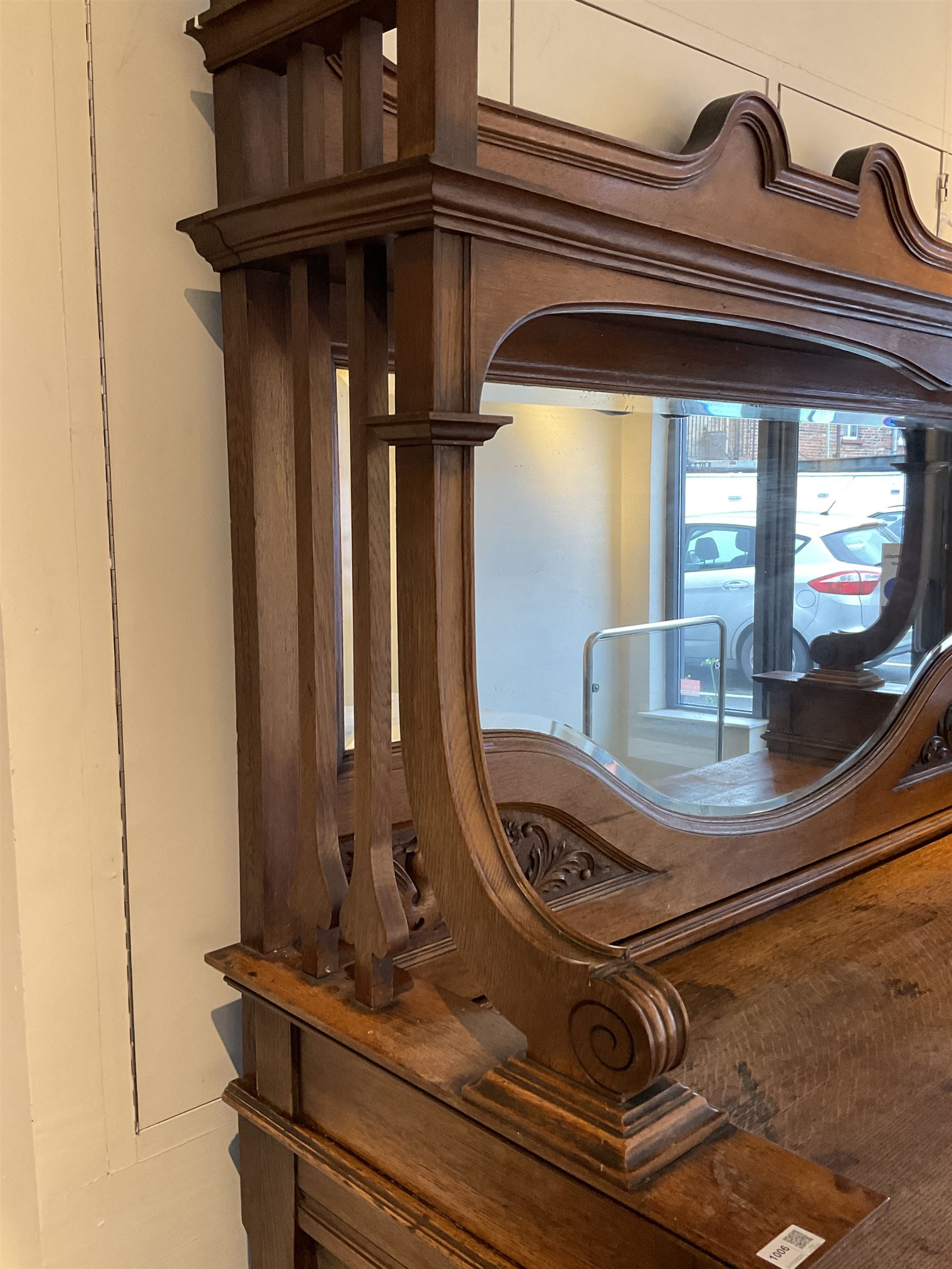 Late 19th century Arts & Crafts period oak mirror back sideboard, shaped bevelled mirror back carved with foliate scrolls and flower heads, down swept supports with elongated club-shaped uprights, moulded rectangular top over two drawers and three cupboards, the drawer fronts with copper handles decorated with sailing ships, panelled doors carved with mythical beasts, flowerheads and foliage, on moulded block feet
