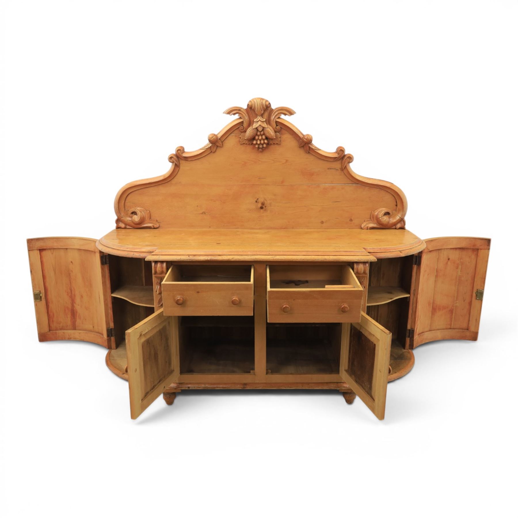 Victorian pine chiffonier, shaped moulded top with raised scroll carved back surmounted by carved fruit and foliate crest, fitted with two frieze drawers over two panelled cupboard doors, the outer cupboards of bowed form, carved foliate corbels, on plinth base