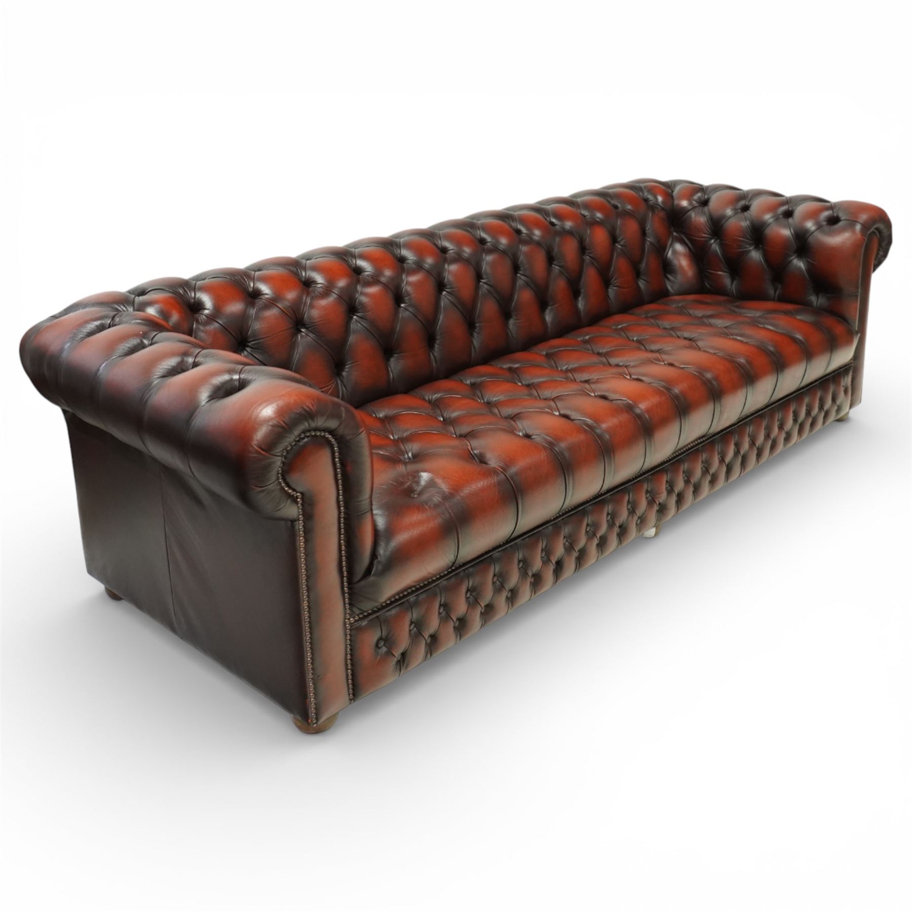 Late 20th century four seat Chesterfield sofa, upholstered in deep buttoned brown leather, with rolled arms, buttoned back and seat, studded detailing and squat feet