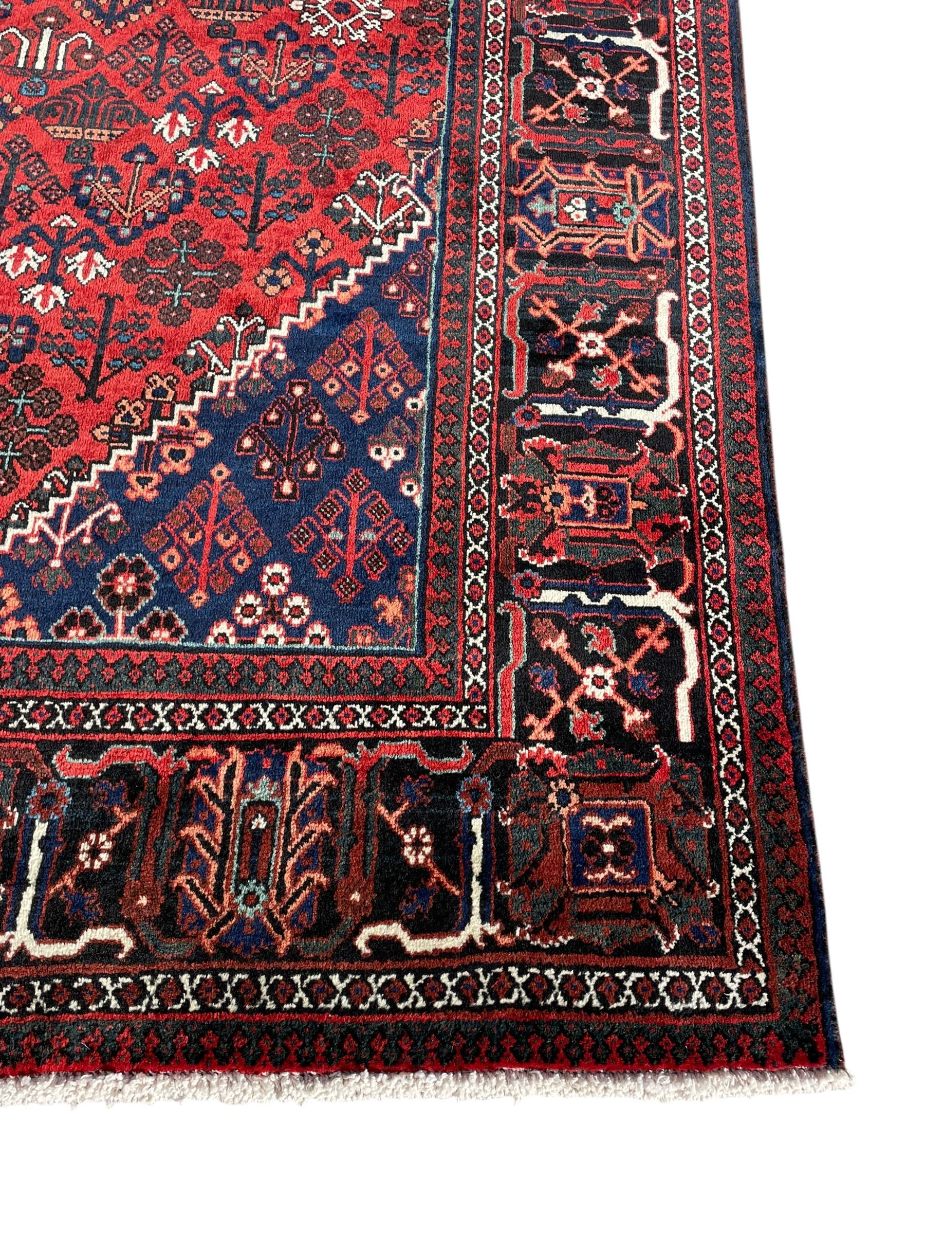 Persian Joshaghan crimson ground rug, stepped lozenge medallion surrounded by repeating foliate lozenge motifs, the border decorated with stylised plant motifs, within geometric guard stripes