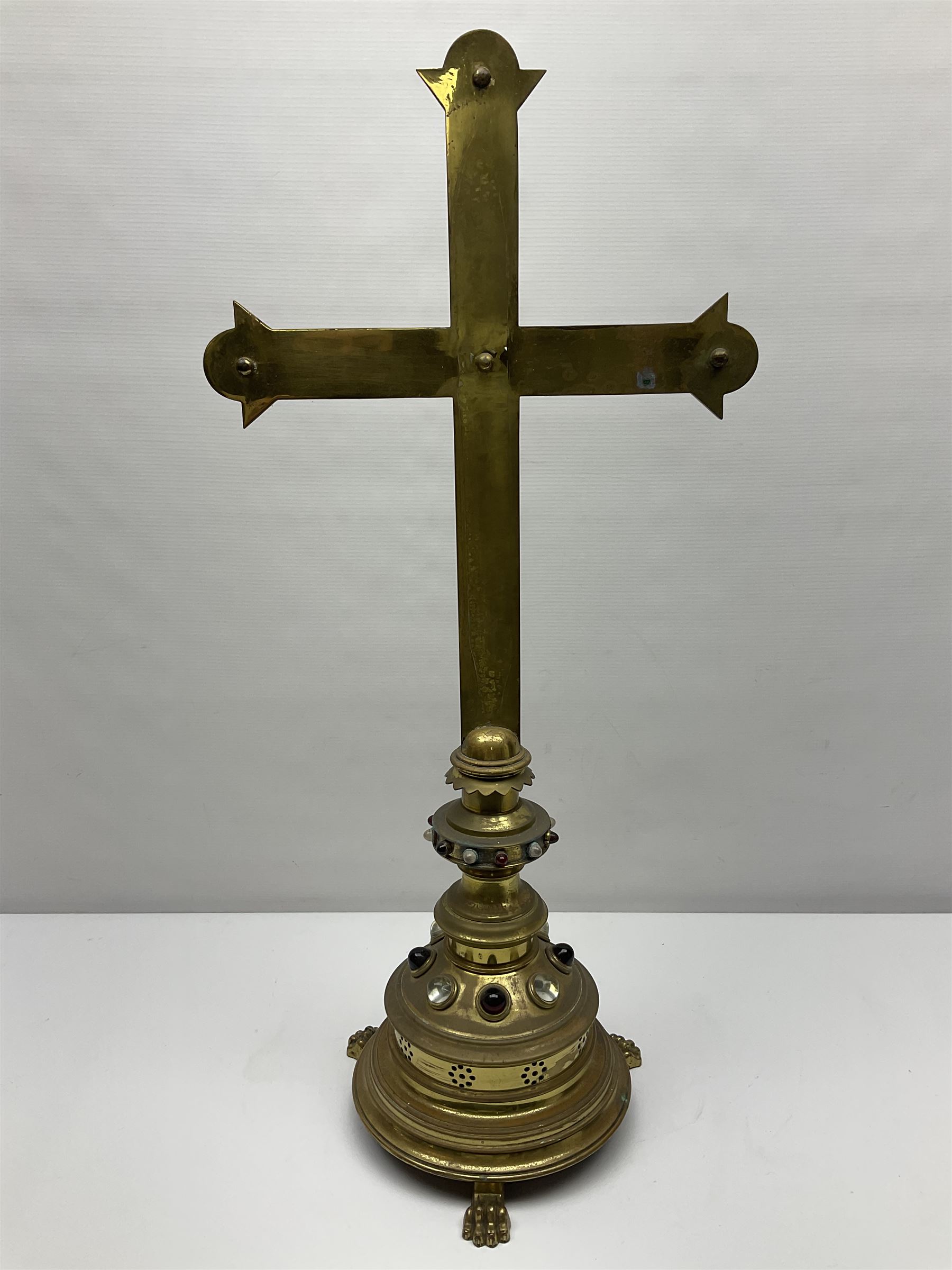 Brass alter cross, decorated with glass cabochons, upon a acicular stepped base and three claw feet, H73cm 