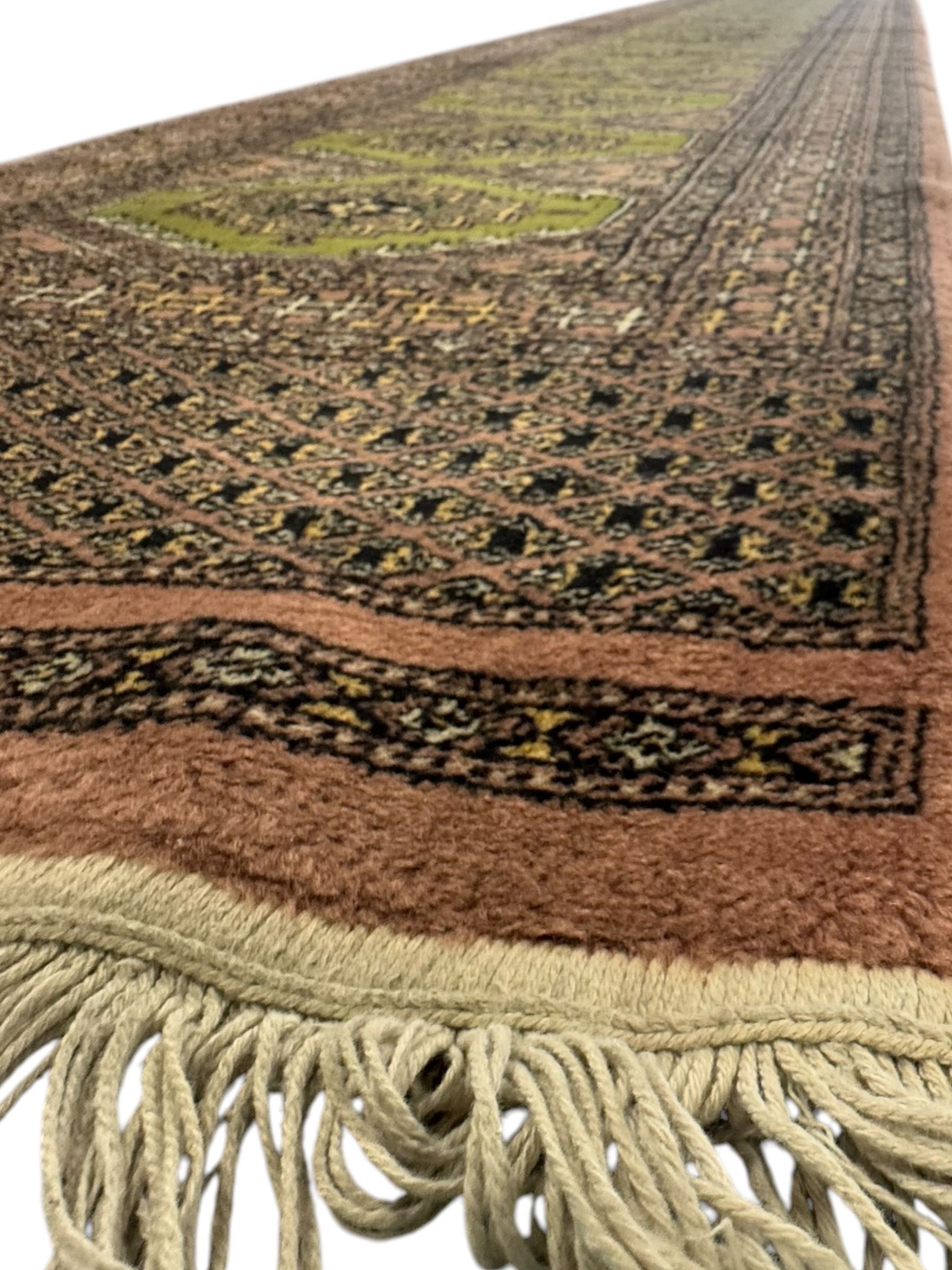 Pakistani olive and rose ground runner rug, the field decorated with repeating hexagonal medallions, surrounded by a rose-hued field with repeating diamond patterns, the borders featuring geometric motifs and trailing foliate designs