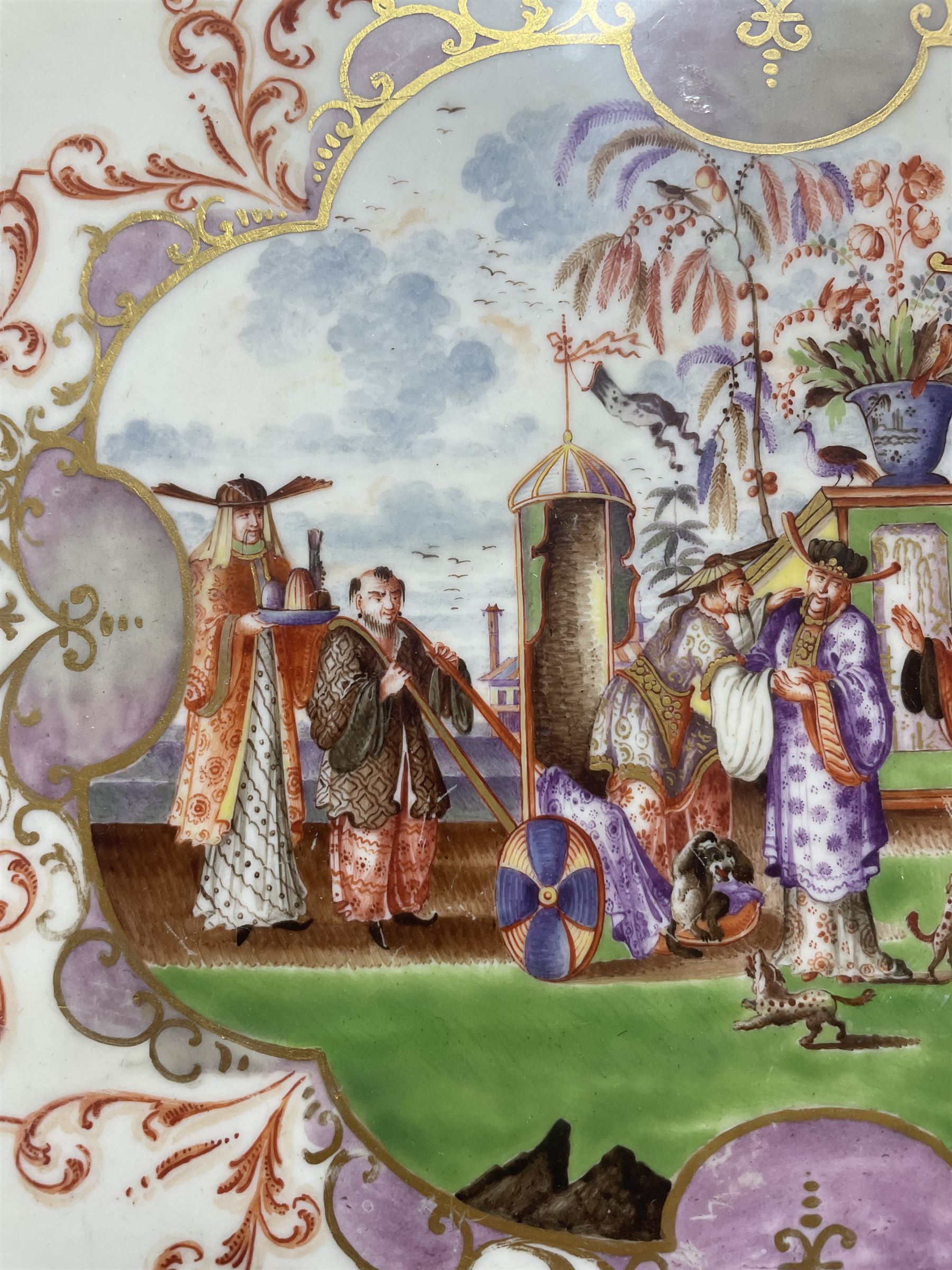 Large and impressive 18th century Meissen dish, finely painted with a chinoiserie scene to a central shaped reserve, depicting figures and attendants engaged in various pursuits, the reserve with gilt scrollwork edge, filled with Böttger lustre and detailed with iron red scrollwork, surrounded by flower heads, the rim with four quatrofoil Kauffahrtei scene panels of merchants and figures by a quayside in purple monochrome, with gilt scroll border, with under glazed blue crossed swords mark, and gilt gilders mark, D39cm
