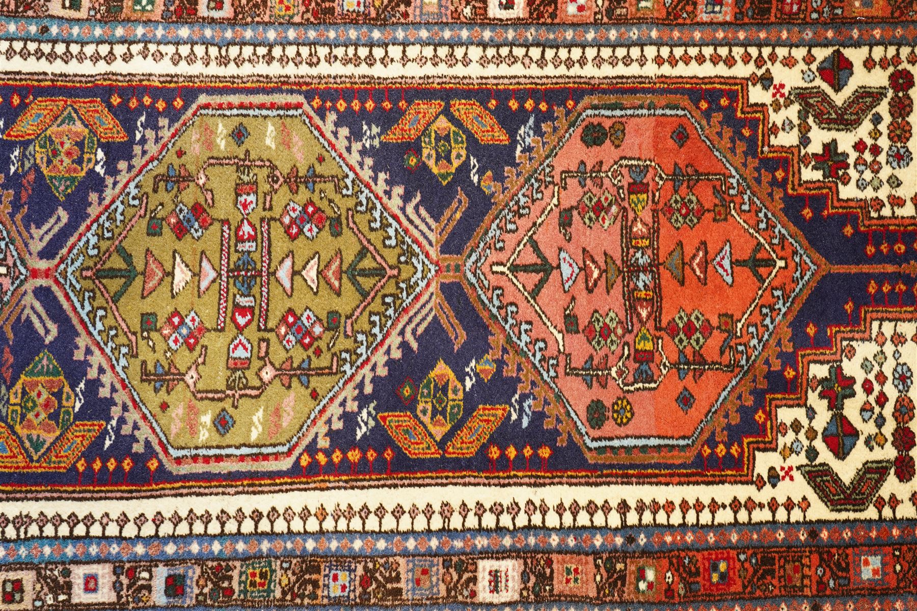 Persian Iranian wool runner, with a series of stepped hexagonal medallions in rust, olive and ivory against and deep navy field, the medallions are filed with floral and latch-hook motifs, framed by and ivory guard border with geometric rosettes, flanked by a rust outer band