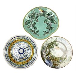Majolica plate decorated with yellow and brown bird upon fruiting holly branches on teal ground with mustard rope twist border, together with two other plates to include a Faience style example, D27cm