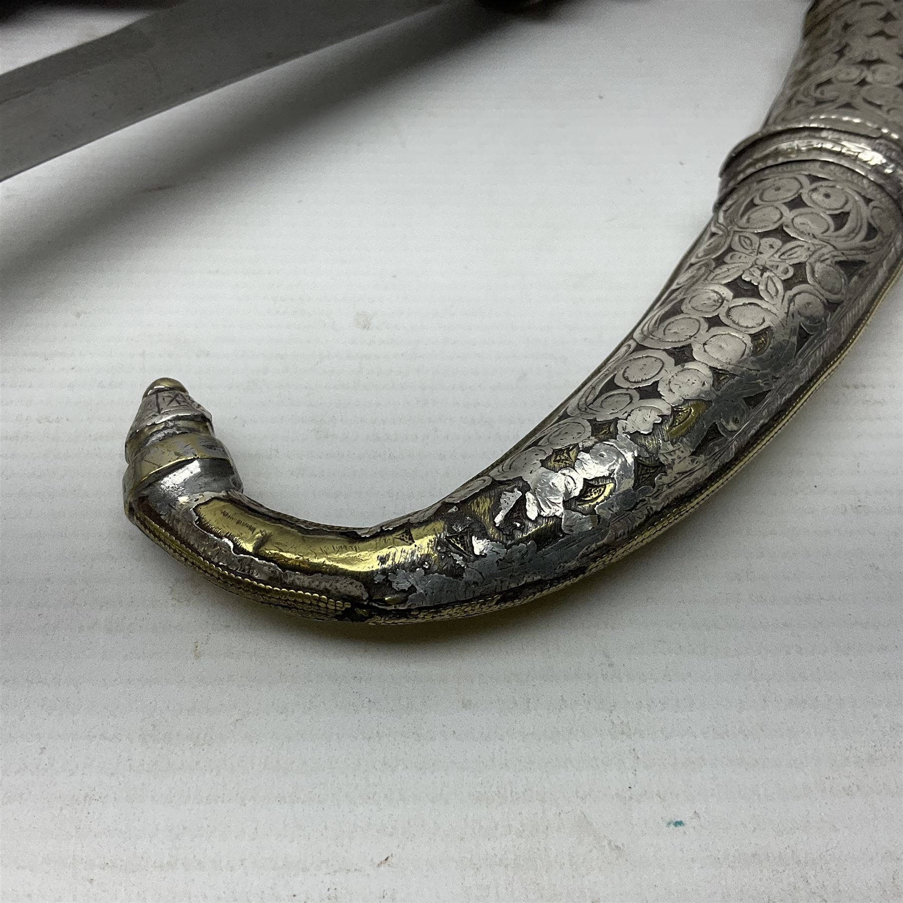 Moroccan jambiya dagger with 24.5cm plain curved blade stamped LONDON to the ricasso area, the hilt and scabbard overlaid with plain sheet brass to the back and ornate silver coloured metal to the front; waisted grip and arched pommel; two pyramid mounts to the scabbard L41cm overall; large billhook with curving blade and stacked leather washer grip; and a reproduction halberd blade (3)