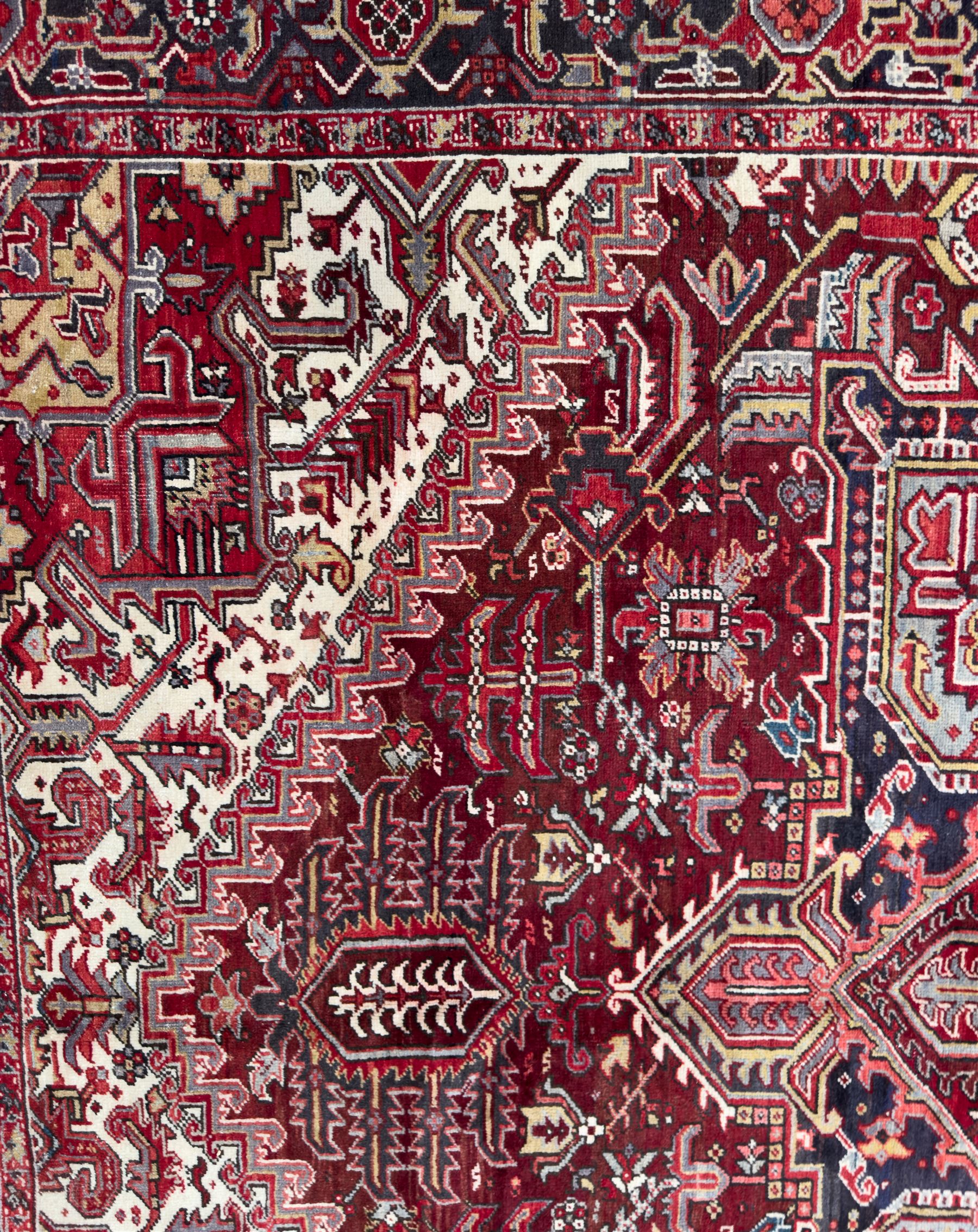 Northwestern Persian Heriz carpet, the madder red field centred by a large octofoil medallion with serrated edge, flanked by ivory stepped spandrels and geometric floral motifs in indigo, ochre and sky blue, enclosed by a navy border of rosettes and angular vines, from the region of Heriz