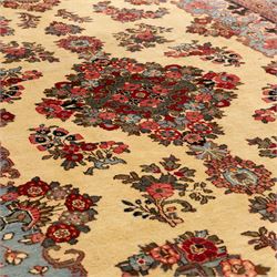 Central Persian Kashan hand-knotted carpet, cream ground, with a central lobbed floral burgundy, rose, and indigo medallion, surrounded by scrolling sprays of carnations and palmettes, with sky blue spandrels decorated with curvilinear vines and stylized blossoms, framed by a repeating terracotta border of palmettes, framed by narrow guard stripes 
