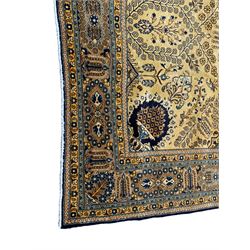 Persian Qom pale gold ground rug, profusely decorated with intricate patterns, lozenge central medallion decorated with trailing leaves and flower heads, surrounded by curled leaf branches and flower head motifs, the spandrels decorated with floral urns, multiple band border, the main band decorated with repeating geometric and flower motifs