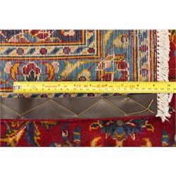 Persian Kashan hand-knotted carpet, madder red ground centred by shaped dark navy, ivory and pale blue floral medallion with pendants, surrounded by scrolling vines, palmettes and flowerheads, dark navy spandrels, enclosed by dark navy floral border with multiple floral guard stripes