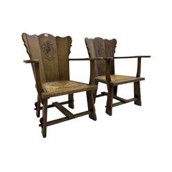 Pair Arts and Crafts oak armchairs, shaped cresting rail and back with carved and painted Heraldic crest, swept arms over drop-in rush seats, raised on shaped stile supports united by peg stretchers