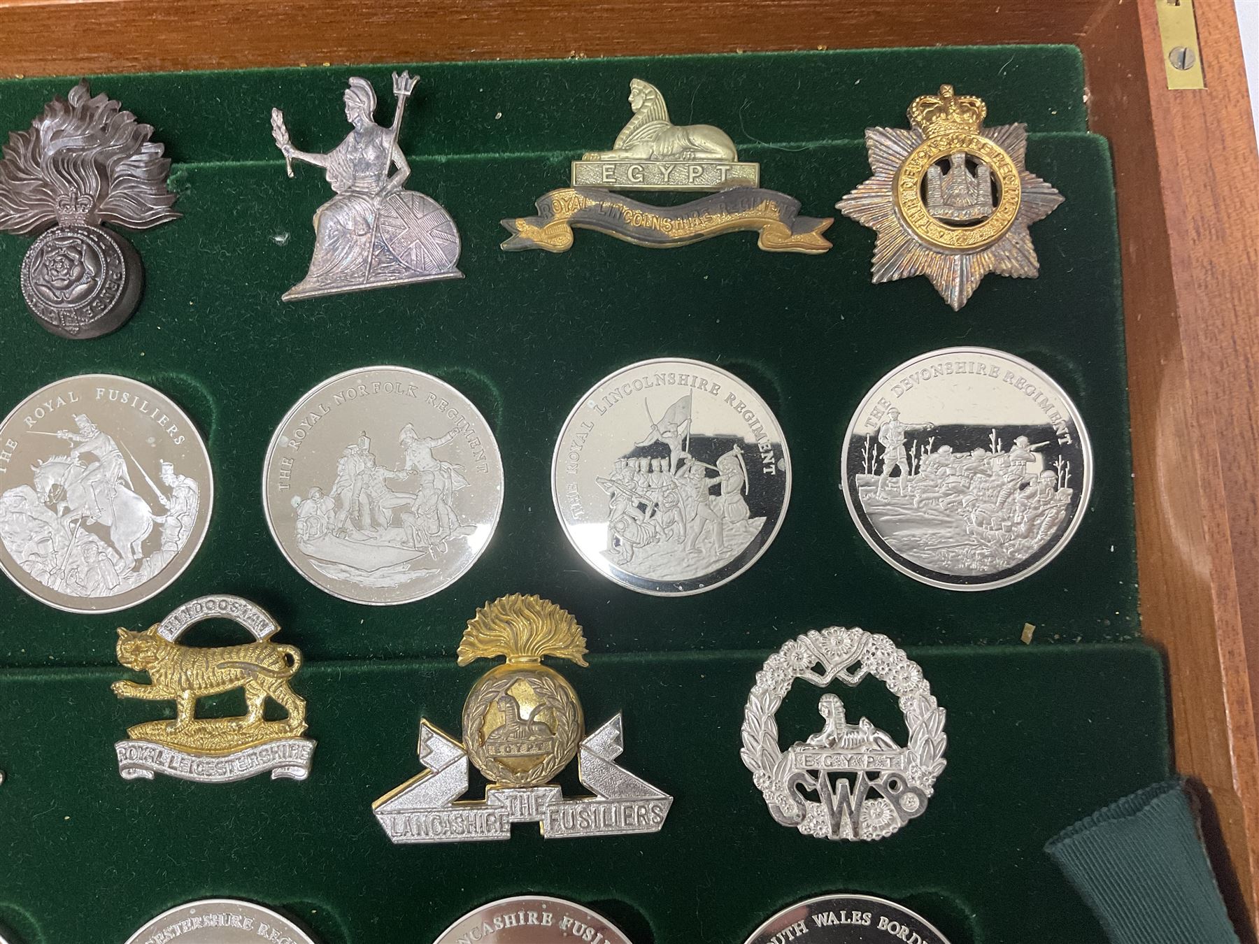 Great British Regiments, 1977, set of fifty two frosted silver medals by the Birmingham Mint, each bearing the name of a regiment with a depiction of an action on the obverse and further details on the reverse, all hallmarked Birmingham Mint, assay offices and dates; together with 52 base metal copy cap badges for each regiment, all housed and mounted on two trays and contained within a wooden presentation case, with brass plaque and fittings, lock and key, with a certificate of authenticity 
