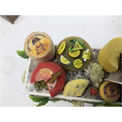 Collection of miniature dolls house grocery shop furniture and produce, comprising glazed corner counter with brass style cash register, shelved preserves unit, pies, cheese board and trays of meats, pair of white cheese counters, biscuit display with six tins, glazed preserves cabinet, pair of shop chairs and four further cheese boards complete with grapes and label flags