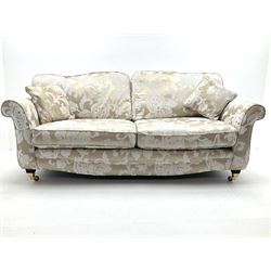 Three seat sofa upholstered in a pale gold ground fabric with floral pattern, shaped cresting rail, scrolling arms