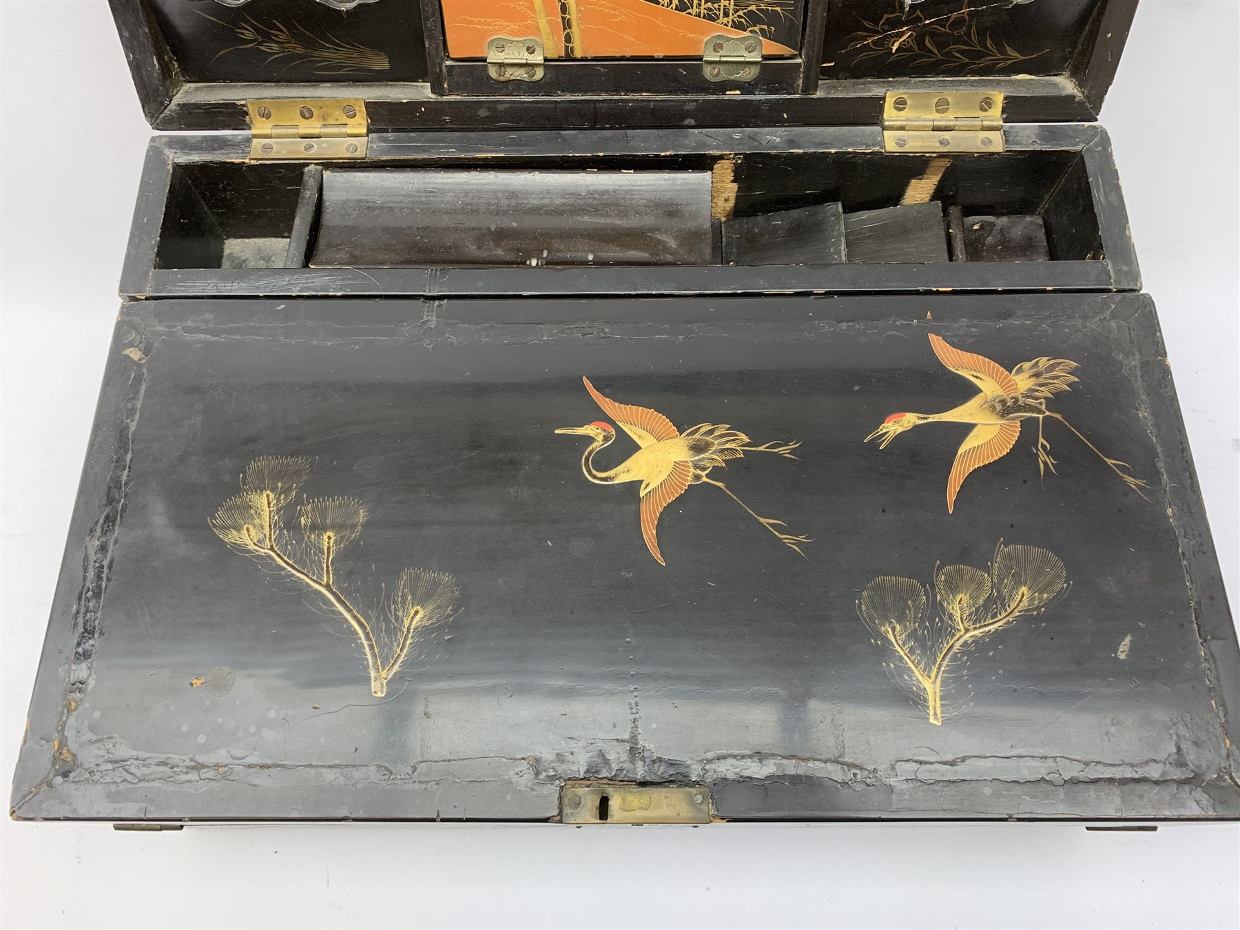  A 20th century Chinese black lacquer and gilt detailed writing box, decorated with figures, pagodas and cranes amidst a mountainous landscape, the hinged cover opening to reveal a compartmented interior and fold out baize lined slope, H20cm L46.5cm D31.5cm.   