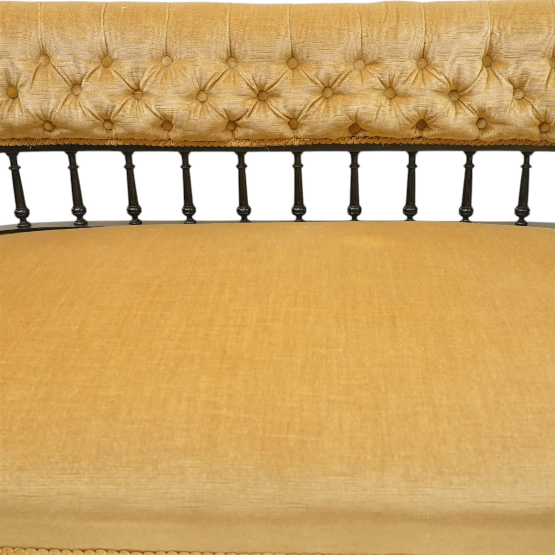 Late Victorian Aesthetic Movement settee, with buttoned upholstered roll-over back and arms, open spindle gallery frame with turned uprights, stuff-over seat, on shaped ebonised supports