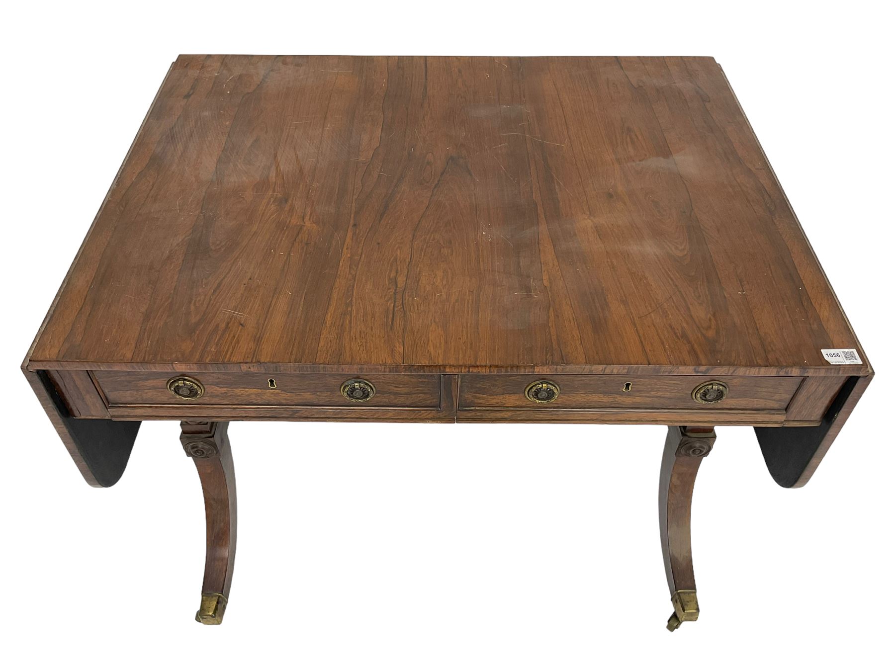 Regency rosewood sofa table, drop leaf rectangular top with rounded corners, fitted with two drawers and two opposing false drawers, raised on dual turned columns terminating in splayed feet united by turned stretcher, on brass cups and castors