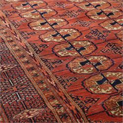 Central Asian Turkmen Tekke hand-knotted rug, madder red field decorated with rows of octagonal guls linked by secondary motifs within a dense geometric border, with fringe ends  