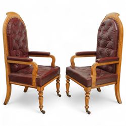 Impressive pair of mid-Victorian oak throne or hall chairs, arched backs on fluted supports with a deep buttoned upholstered panel and upholstered curved arms over fluted seat rails and tapering turned front legs with original brass and brown porcelain castors, and out-swept rear supports