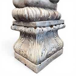 20th century composite stone garden figure, modelled as a kneeling nude female with arms raised behind her head, mounted on an integral cushion, the squared ogee pedestal moulded with acanthus leaves and flower heads, in a white painted and weathered finish