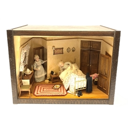 A 1/12th scale diorama of a cottage bedroom, depicting an elderly couple, he in bed, her by the door with cup in hand, the interior furnished with wash stand, wash jug and bowl, needle work, brass bed, and mouse trap under chair, plus light up candle and ceiling pendants, etc., H29cm L40cm D26cm.

