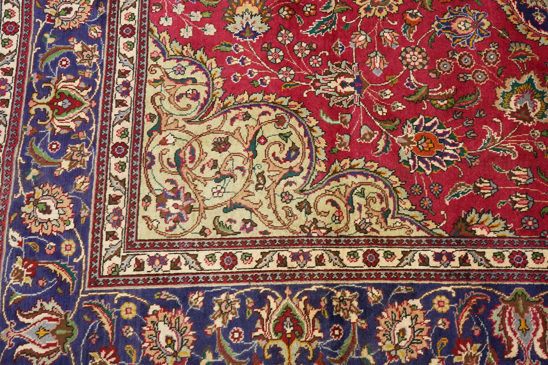 North East Persian Meshad hand-knotted carpet, crimson field with central lobed medallion in tones of indigo, ivory and soft blue, with an all-over arrangement of scrolling vinery, palmettes, and floral  sprays, conforming spandrels, main border of stylized floral vinery framed by multiple guard borders, with cotton fringe ends