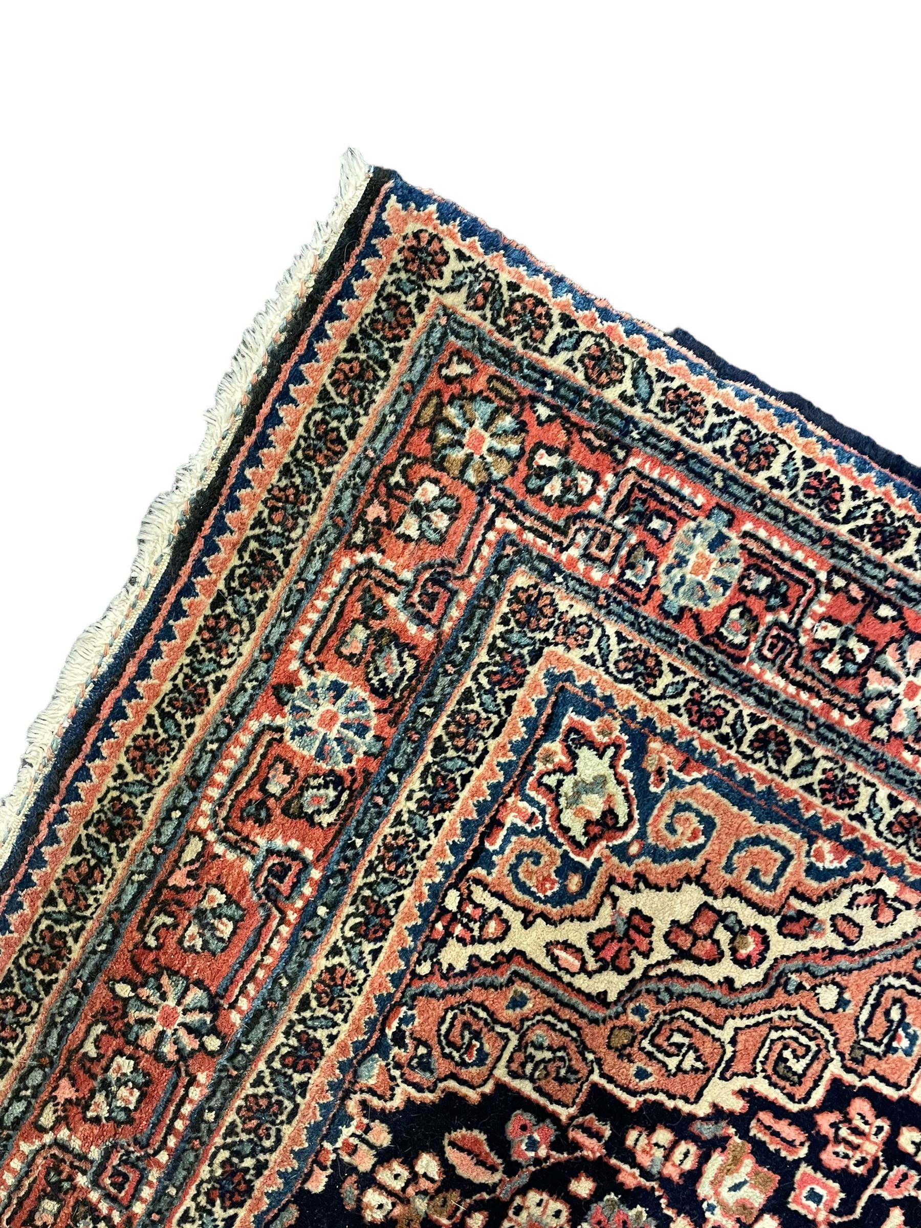 Persian indigo ground rug, the field decorated with intricate interlaced foliage branches and small flower heads, shaped floral design central medallion, the border decorated with scrolling branch and flower heads within guard bands 