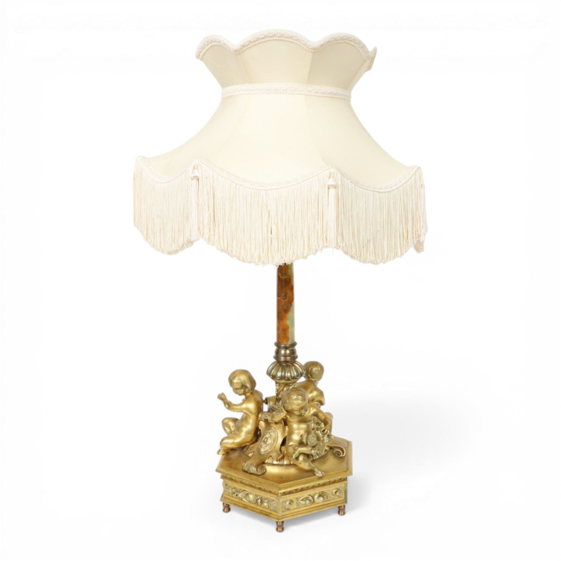 Second Empire style gilt metal table lamp, the hexagonal plinth base with applied foliate decoration, upon six turned feet, supporting three seated allegorical putti, the first modelled with a tablet and stylus representing literature, the second with hammer representing sculpture, and the third with Corinthian column capital representing Architecture, each intersected by a stylised scroll with central flower head panel, mounted upon an onyx and gilt metal Corinthian column with wrythen flower moulded and part fluted base, supporting a cream octagonal shade, overall H86cm