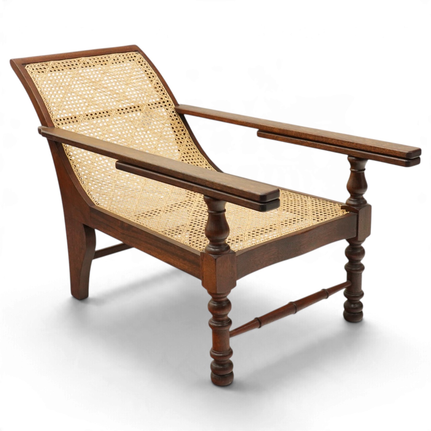 20th century teak framed plantation chair, plain cresting rail over cane back and seat, fitted with hinged extending leg rests, raised on turned front-supports united by ring-turned stretcher