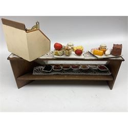 Collection of miniature dolls house grocery shop furniture and produce, comprising glazed corner counter with brass style cash register, shelved preserves unit, pies, cheese board and trays of meats, pair of white cheese counters, biscuit display with six tins, glazed preserves cabinet, pair of shop chairs and four further cheese boards complete with grapes and label flags