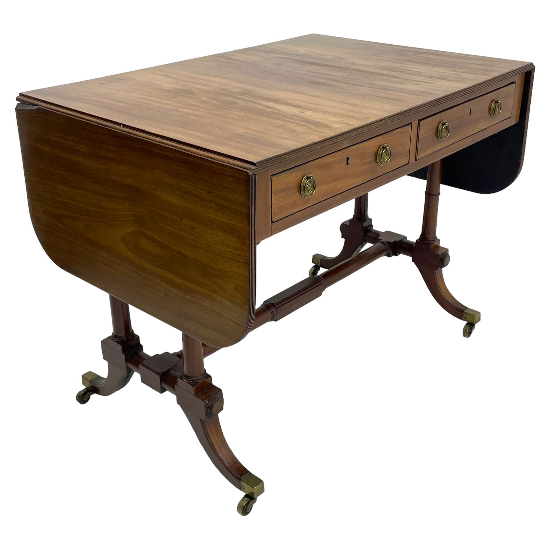 George III mahogany sofa table, rectangular drop-leaf top with reed moulded edge and rounded corners, fitted with two frieze drawers and two opposing false drawers, quadruple collar turned pillar supports on turned and block platforms, splayed and moulded supports with brass cups and castors 