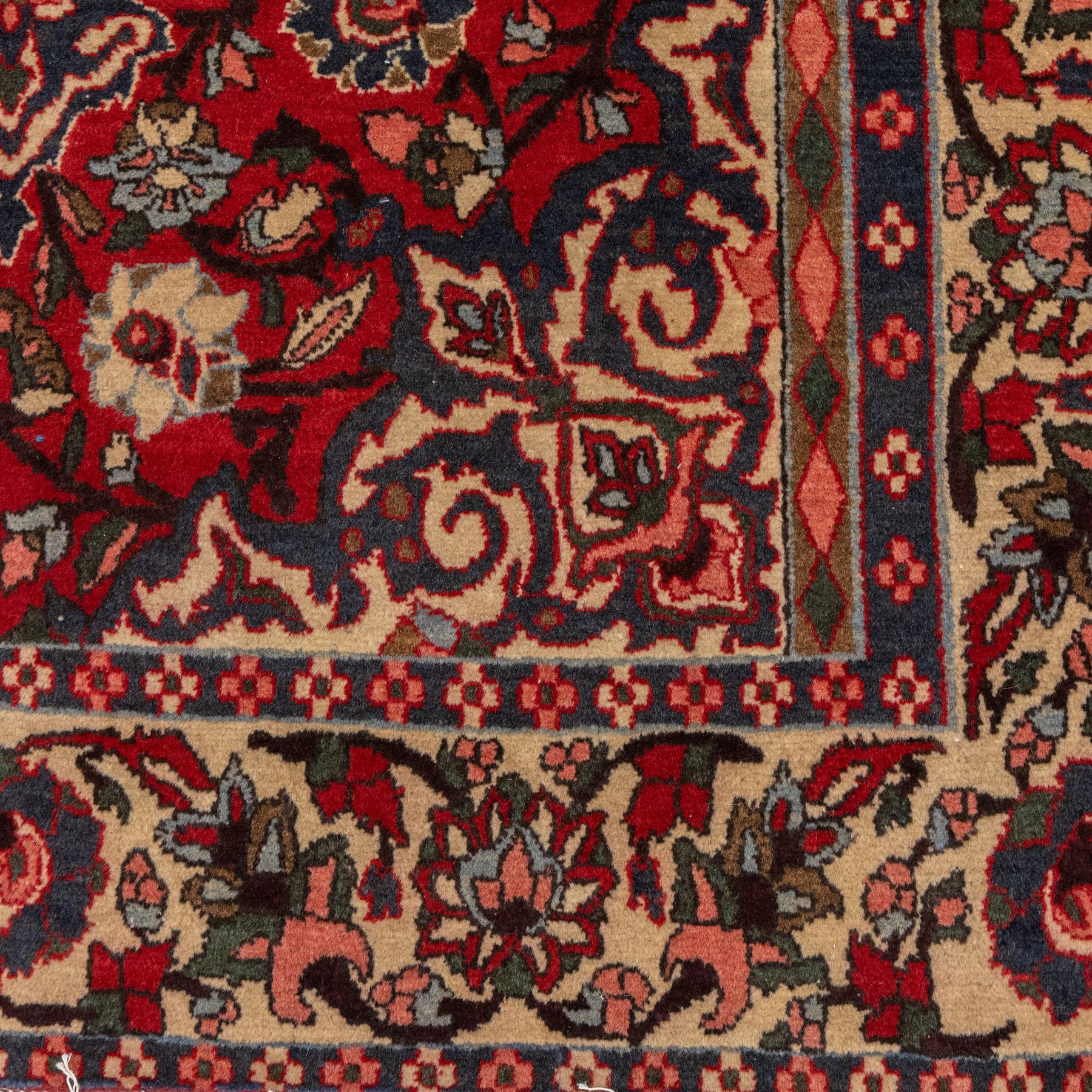 Central Persian Isfahan hand-knotted rug, madder red field, with elaborate central medallion with pendants and scrolling arabesques, palmettes and stylized floral sprays arranged in a densely ornamented ground of classical Safavid inspiration, ivory border with a continuous vine scroll of palmettes and rosettes, flanked by multiple guard stripes in navy and red with geometric and floral motifs, with cotton fringe ends 