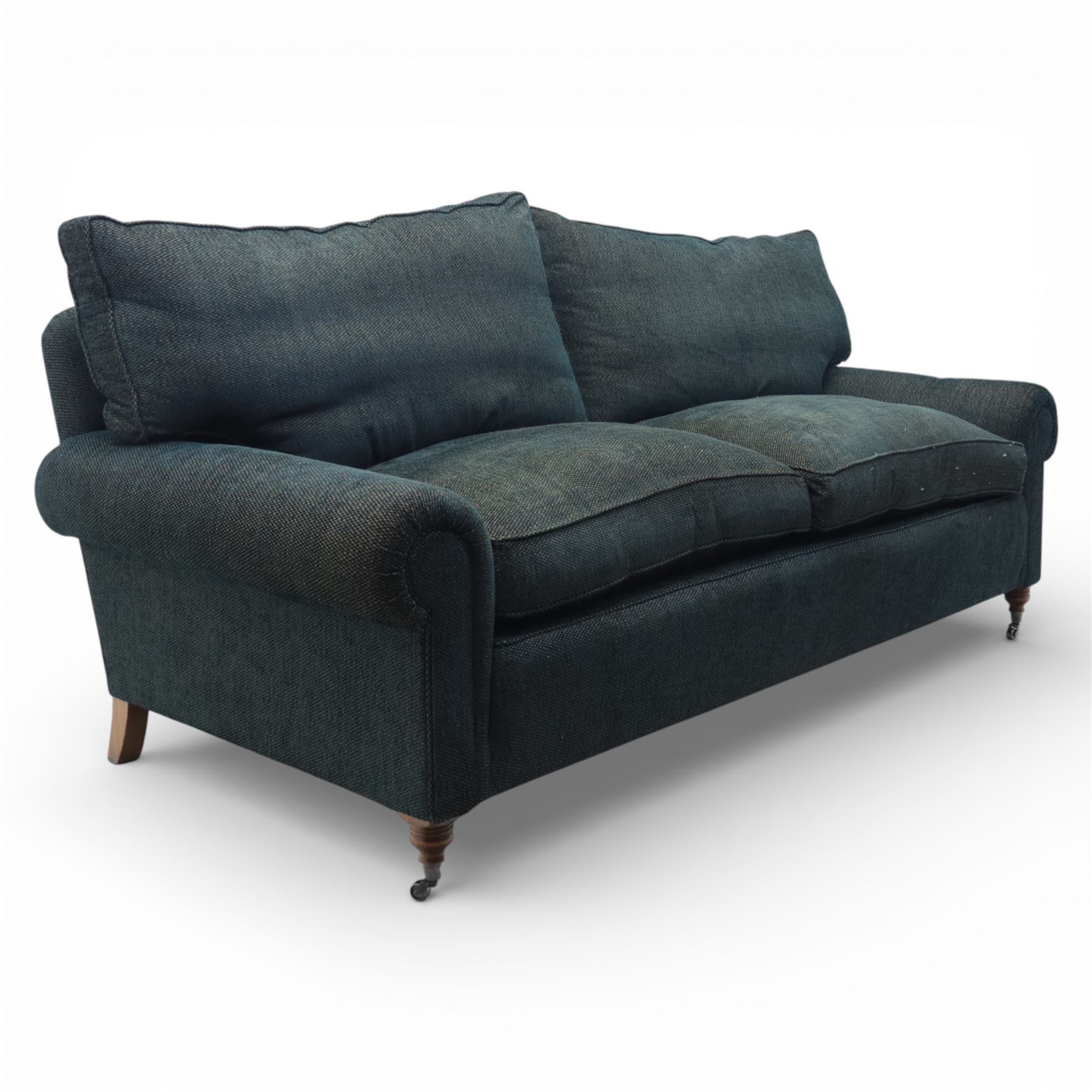 Late 20th century three seat sofa upholstered in green fabric, with gently rounded scroll arms, loose seat and back cushions, raised on turned wooden legs with castors, rear splayed legs
