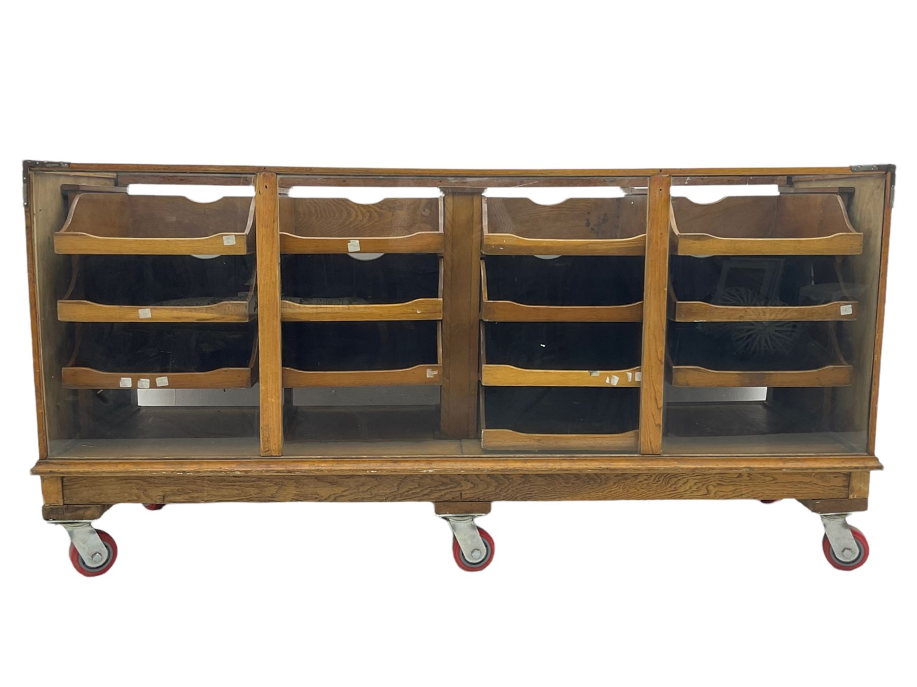 Early 20th century oak framed and glazed haberdashery / shop display cabinet, fitted with sixteen drawers (three missing), on later casters