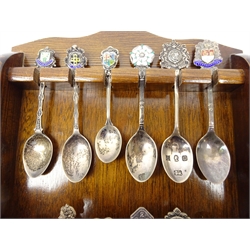  Collection of commemorative & crested silver and enamel teaspoons and one silver-plated, displayed on oak spoon rack   