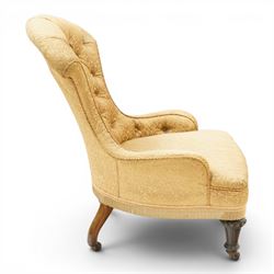 Victorian Aesthetic Movement walnut framed nursing chair, the fan back and sprung seat upholstered in buttoned foliate patterned gold damask fabric with fringing, raised on beaded tapering fluted supports with ceramic castors