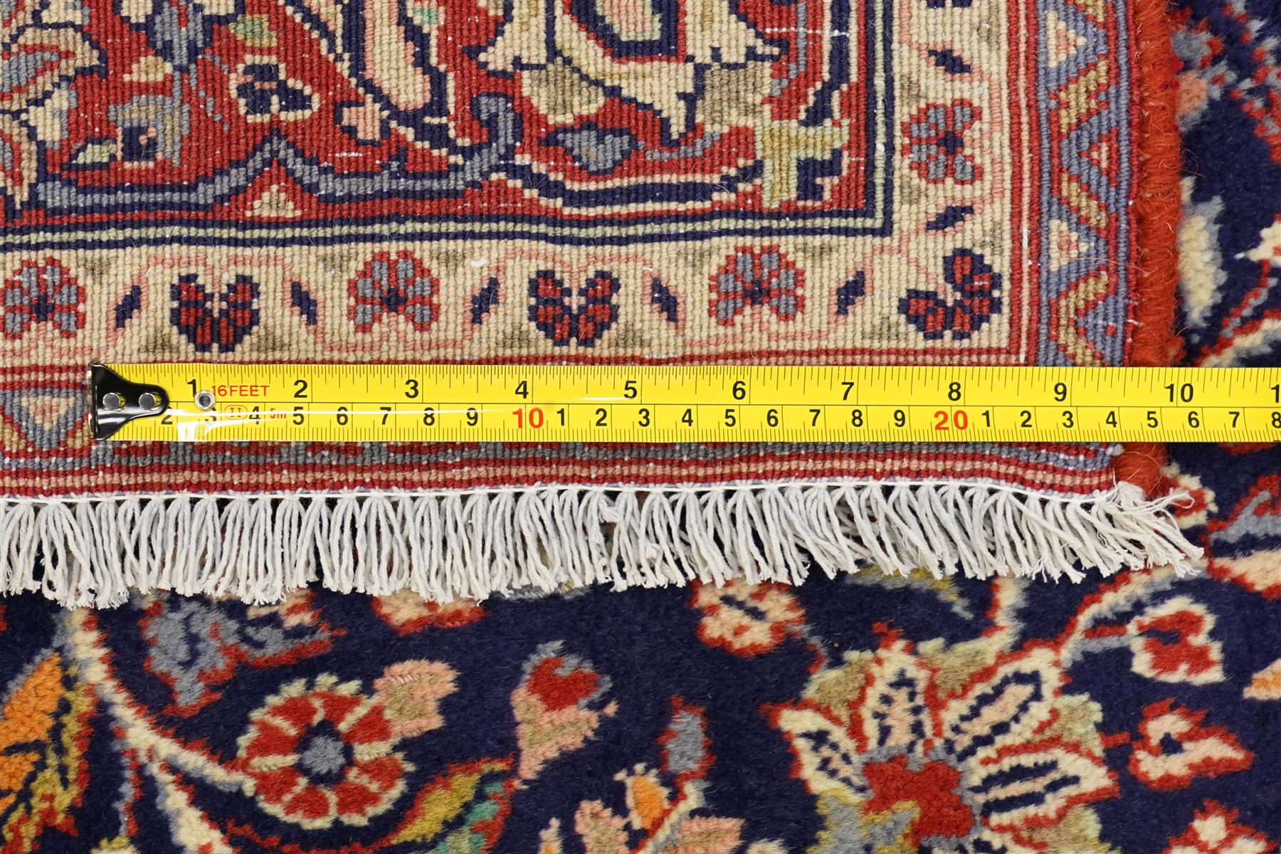 Central Persian Kashan hand-knotted rug, indigo field with central lobed medallion with pendants issuing scrolling arabesque of palmettes, flowering vines, and foliate tendrils, with conforming spandrels, with vine border and framed by guard stripes in tones indigo, ivory and madder red, with cotton fringe ends 