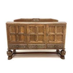 Early 20th century oak sideboard, raised back featuring carved detail, three panelled cupboard doors enclosing fitted interior, above three long drawers, raised on carved cup and cover supports to meet stetcher