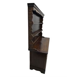 Late 19th century oak dresser, the upper section with two shelves beneath a shaped cornice, the lower section with a central bank of three drawers flanked by cupboard doors, all decorated with geometric diamond motifs, the drawers fitted with brass handles, raised on a shaped plinth base