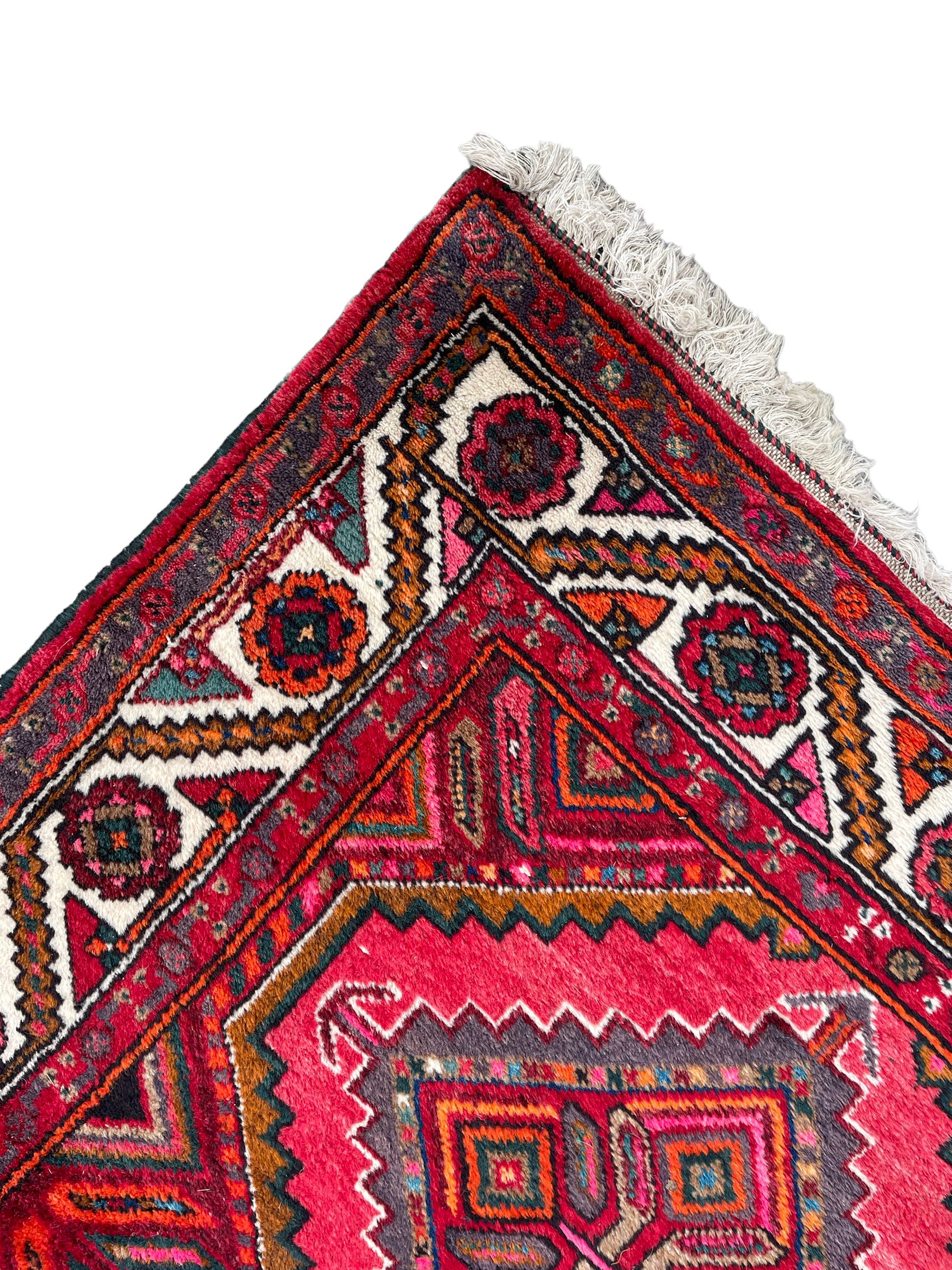 Persian Hamadan red ground rug, decorated with six stepped lozenge medallions, the guarded border with repeating stylised flower head decoration, with inscription to corner