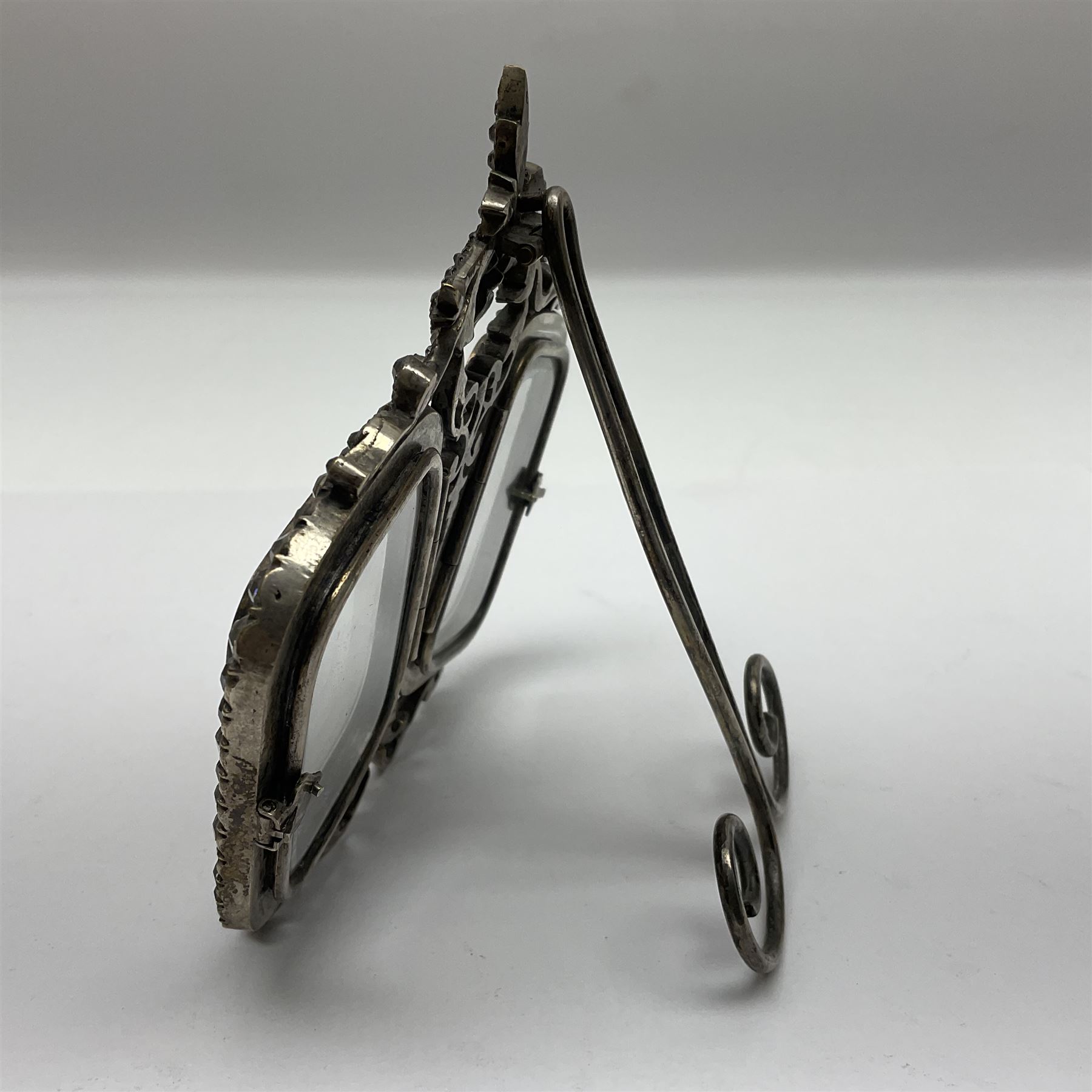 Early 19th century silver plated double photograph frame, each rounded rectangular aperture surrounded by a paste border, with ornate scroll feet and mantling also set with clear paste stones, with easel style support verso, H12cm