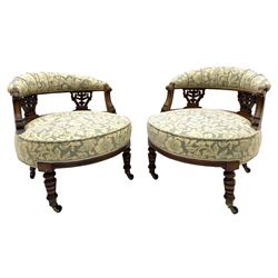 Edwardian walnut three piece drawing room salon suite - pair tub shaped occasional chairs and nursing chair, upholstered in cream and pale blue fabric decorated with floral pattern, pierced and foliate carved splats, curved sprung seats, the nursing chair with buttoned back rest, turned supports with brass and ceramic castors, recently reupholstered by Peter Silk of Helmsley