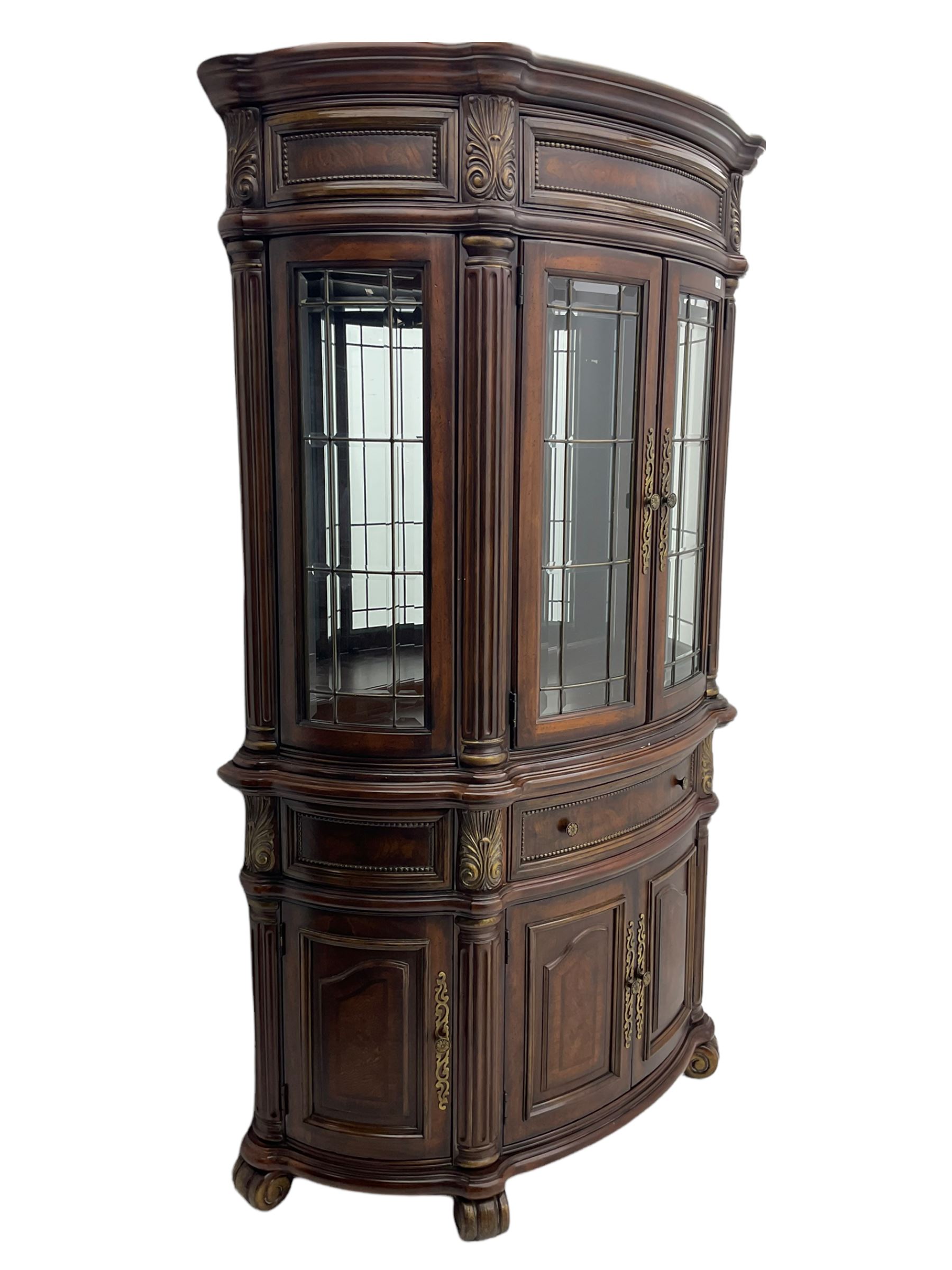  Kevin Charles American walnut demi lune display cabinet with illuminated interior, projecting cornice, two bevel edge glazed doors enclosing two adjustable shelves above single drawer and four cupboard doors with wine rack, carved scrolling supports