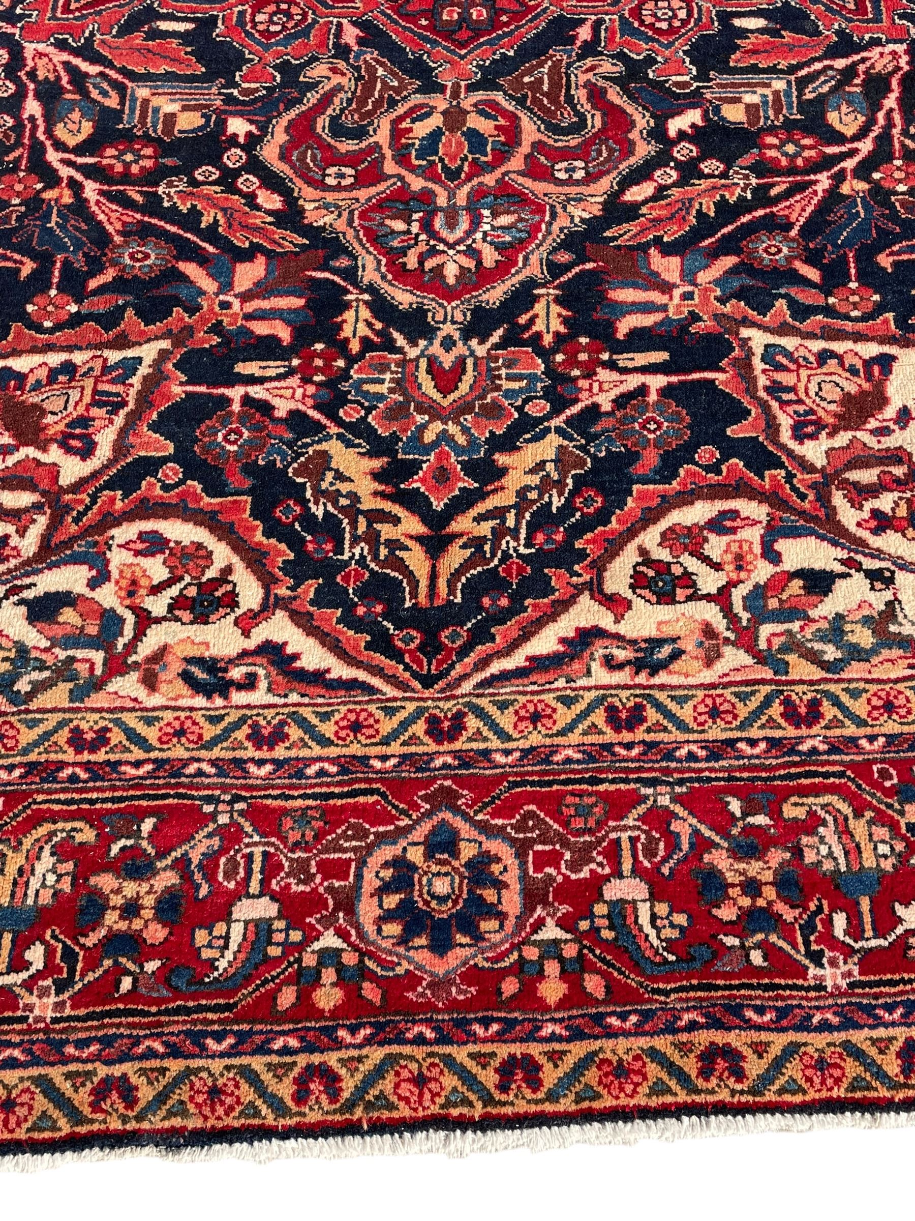 Persian Hamadan indigo and red ground carpet, large central medallion decorated with projecting palmette motifs, the surrounding field decorated with trailing branches and flower heads, crimson ground border decorated with stylised plant motifs, within floral pattern guard stripes 
